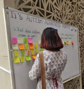 A student putting up a sticky note answering 'What does autism mean to you?"
